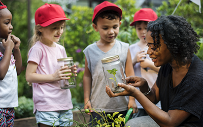A teacher showing a jar with a bug in it to children on a field trip.