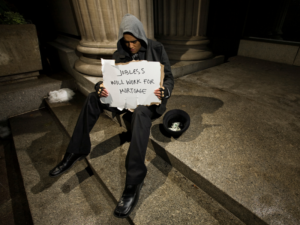 Man on steps holding sign that reads jobless, will work for mortgage