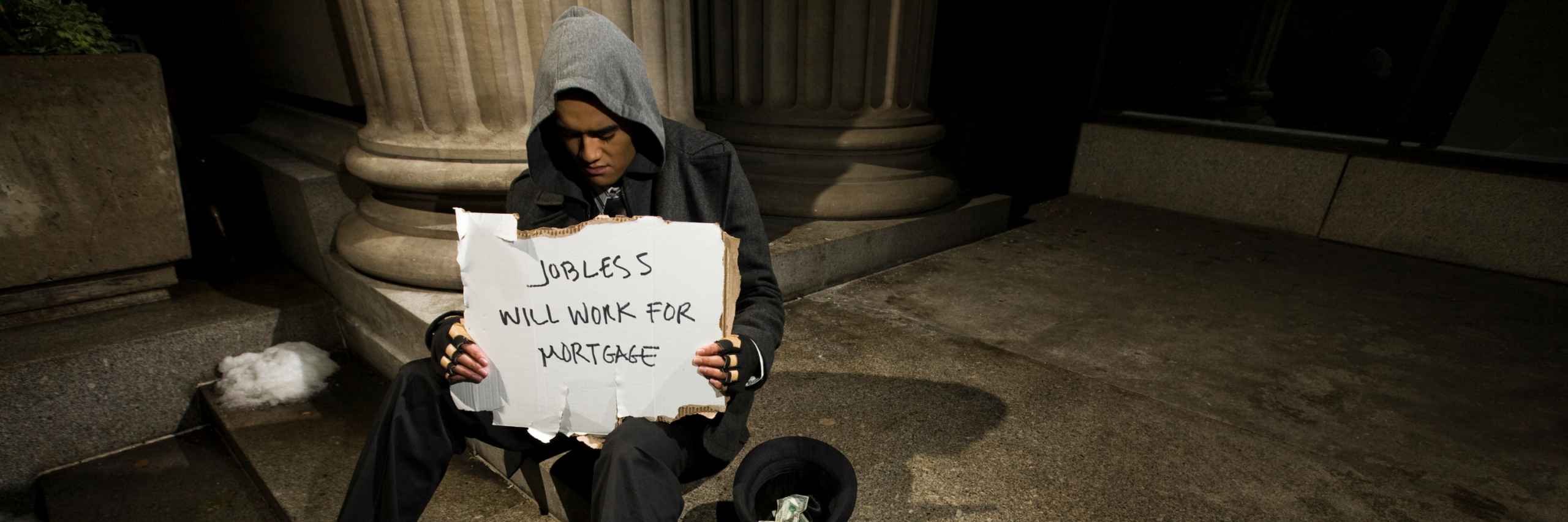 Man on steps holding sign that reads jobless, will work for mortgage