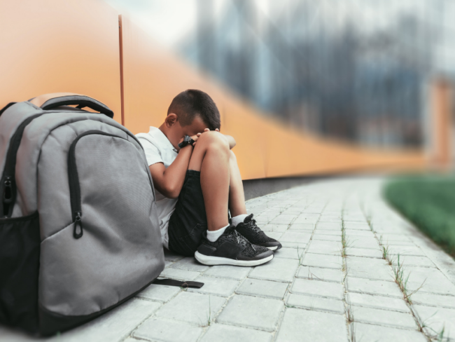 sad kid sitting near book bag