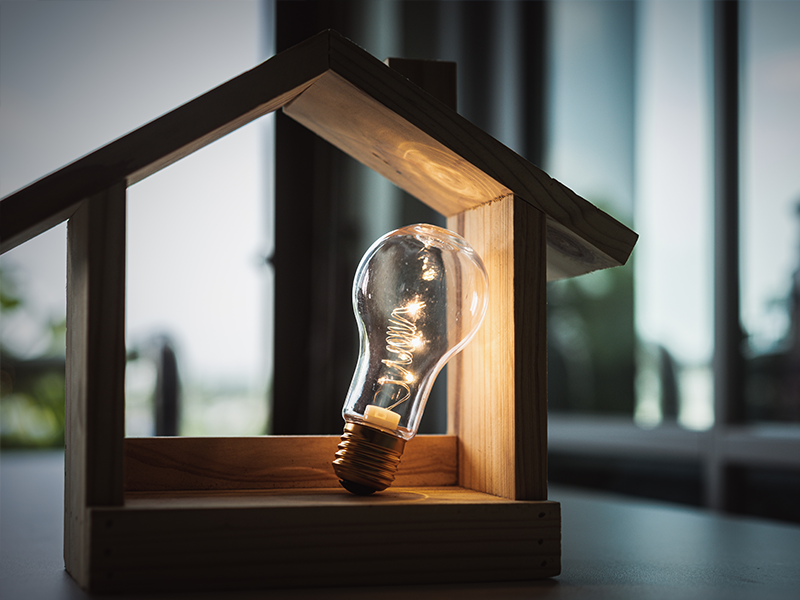 A lightbulb inside of a wooden house frame.