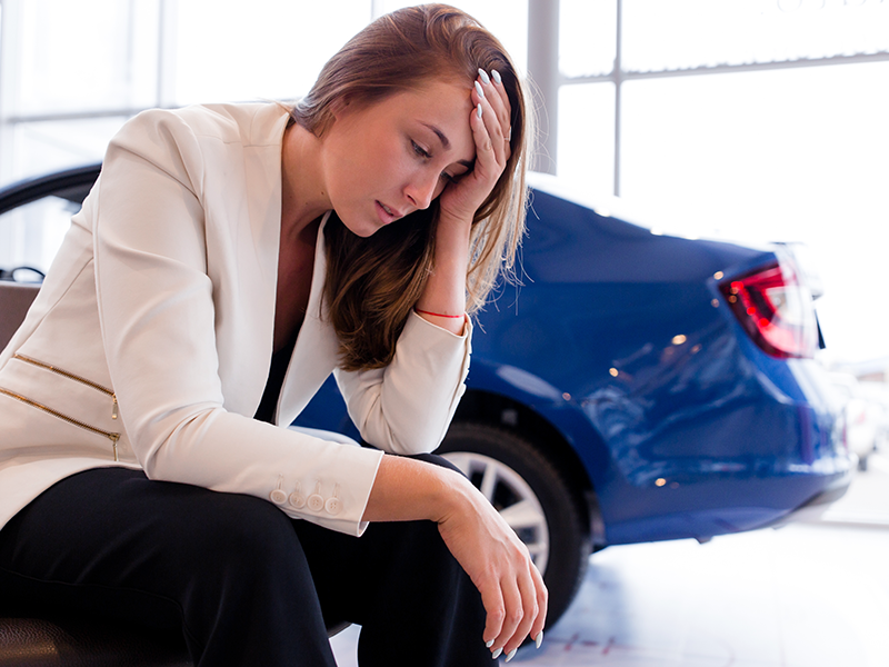 a woman frustrated and holding her head, with a car in the background