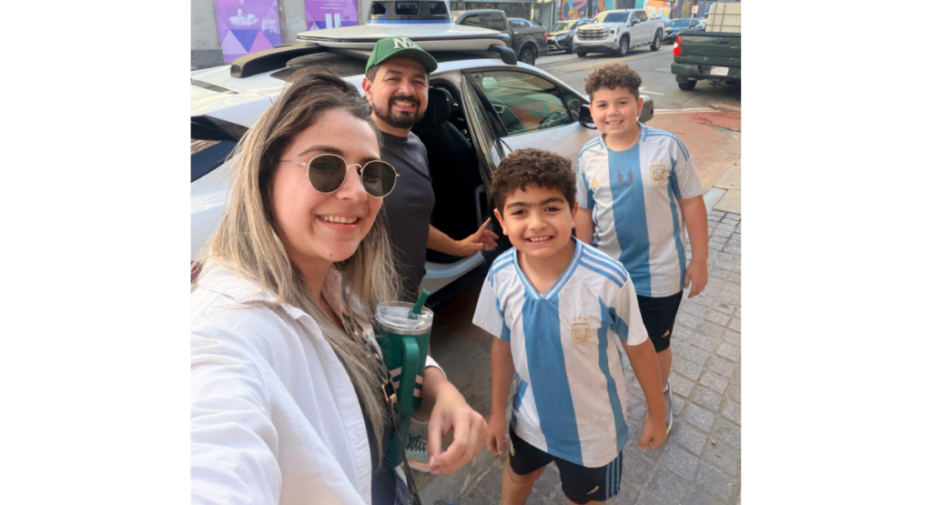 Cesar and his family smile for the camera in front of a car with an open back door.