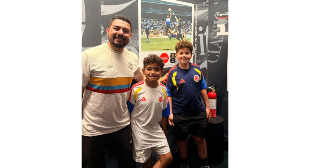 Cesar and his sons stand together in front of an image of a soccer match.