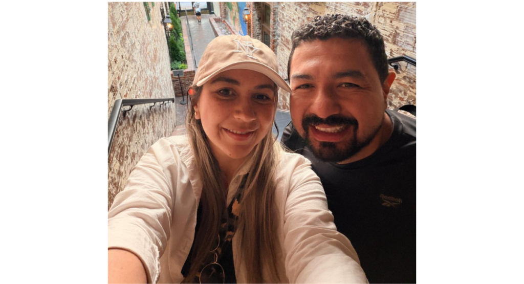 Cesar and his wife smile as they take a selfie on a brick staircase.