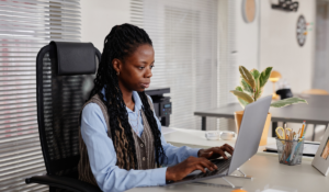 A woman sits at a desk and types on a laptop.