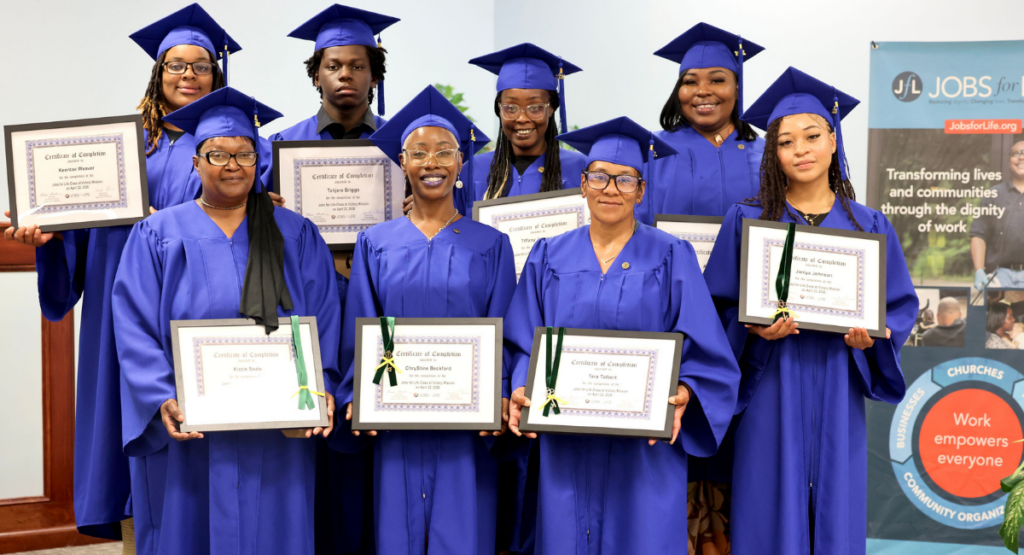 Graduates from the BETTER WORK Program stand in two rows of four students each. They wear caps and gowns and hold certificates of completion. Ayonia stands in the back row at far right.