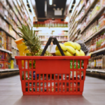 A red shopping basket sits on the ground in the center of a grocery store aisle.