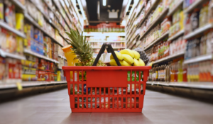 A red shopping basket sits on the ground in the center of a grocery store aisle.